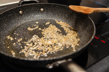 Closeup of shallots frying in a pan with a wooden spoon on a modern hob. 