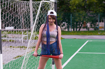 girl with dreadlocks in shorts with a baseball bat on a football field