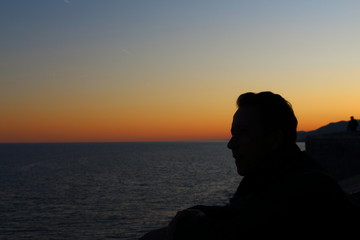 Silueta a contraluz de un hombre pensativo mirando el horizonte del mar durante el atardecer