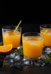 Tangerine cocktails with sliced mandarins, ice, mint on a black wooden table