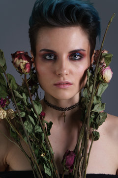 Studio portrait of a beautiful girl with blue hair and a fashion make-up without clothing with bouquet of flowers. Fashion style