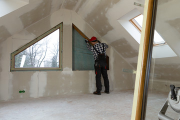 Handyman, construction man installing PVC window in a new insulated and filled dry wall attic.