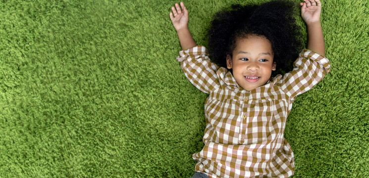 Happy children little girl smiling and laying on green carpet floor in living room at home.