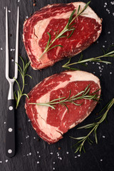 Raw fresh meat Ribeye Steak, seasoning and meat fork on rustic background