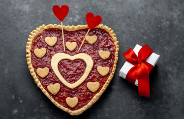 heart-shaped cake with jam and a gift with a red ribbon, on a stone background with copy space for your text. valentine's day celebration concept
