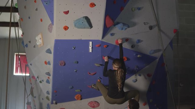Man spotting woman as she climbs up rock wall in gym as they celebrate with each other.