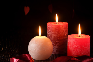 Three wax flame candlelight with ribbon in dark romantic light on hearts background, love dating, Valentine's day, selective focus