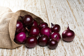 fresh red onions in bag on wooden background.