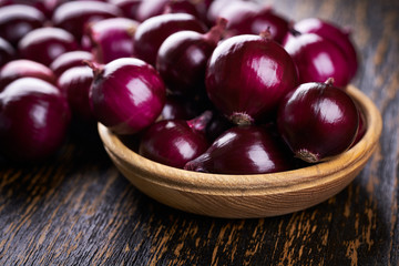 Red onions in wooden bowl on wooden table selective focus.