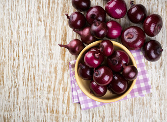 Red onions in wooden bowl on wooden background. Top view.