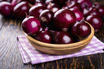 Red onions in wooden bowl on wooden table selective focus.