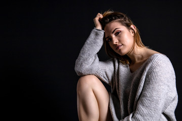 young beautiful girl in a gray sweater with a calm pensive facial expression sits on a dark background, copy space