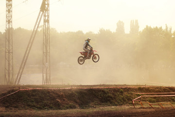Motorcyclist in a motocross competition in a jump on a dusty track with an urban landscape