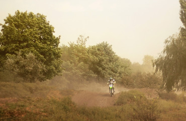 Riding motorcyclist on a dusty road with trees on the sidelines on a motocross