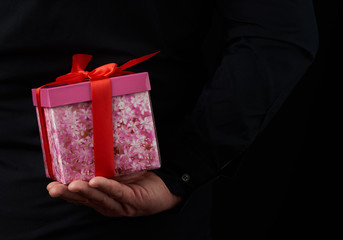male hand holds a paper-wrapped box with a gift behind his back
