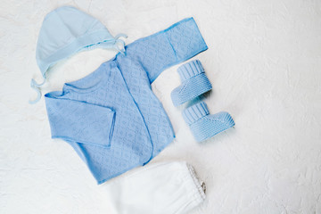 Set of baby boy clothes for newborn on a white background. Blue undershirt, knitted booties, cap and bodysuit.