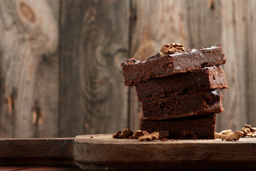 stack of square baked slices of brownie chocolate cake with walnuts on a wooden surface. Cooked homemade food