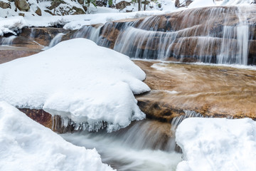 Frozen river in winter at Diana's Baths, New Hampshire. Water flowing over rocks and under snow and icicles.