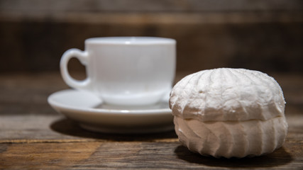 White marshmallows, in a white plate on a wooden table, against the background of white coffee cups.