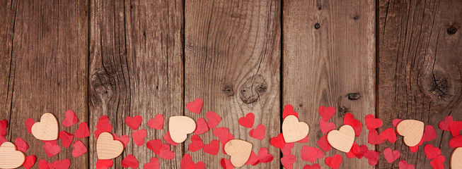 Valentines Day banner with border of wooden hearts and confetti. Above view on a rustic wood background. Copy space.