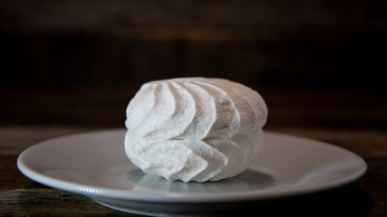 White marshmallows, cake folded into a pyramid, one on one, in a white plate on a wooden table.