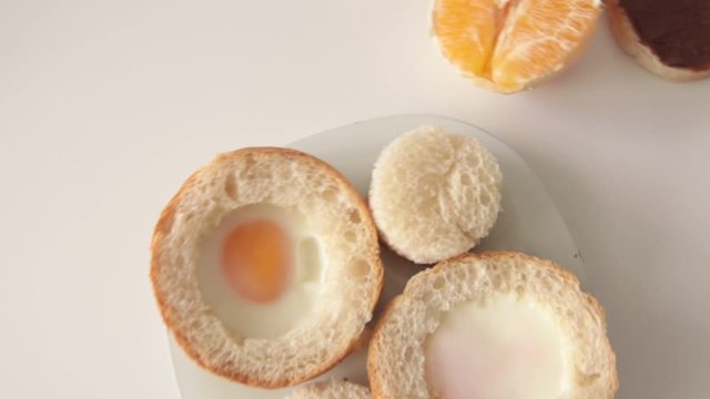 slow motion of the camera on a white table with breakfast on a plate: baked eggs in round buns, half an orange and two slices of bread with chocolate paste