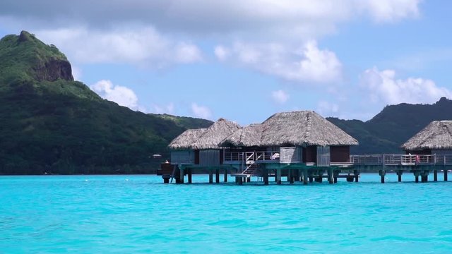 Slow motion drone low angle shot. Bungalows in turquoise blue lagoon with coral reef in Bora Bora, Tahiti French Polynesia. Paradise travel vacation & romantic getaway, honeymoon exotic destin
