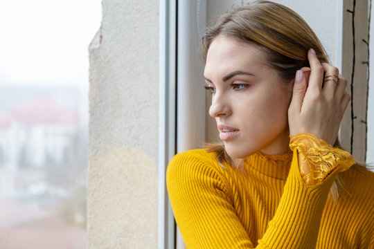 young cute girl in an orange sweater and looks out the window