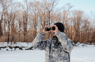 Fototapeta na wymiar traveler in camouflage clothes looking at winter nature through binoculars