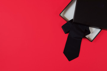 classic men's black tie inside a black  gift package on a red background. top view, space . perfect valentine's day for men's gift. 