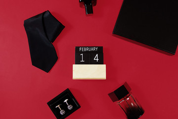 Composition of black neck tie, arm buttons, two perfumes and a gift box  on red  background. Top view. Man's fashionable style concept. Gift for men.
