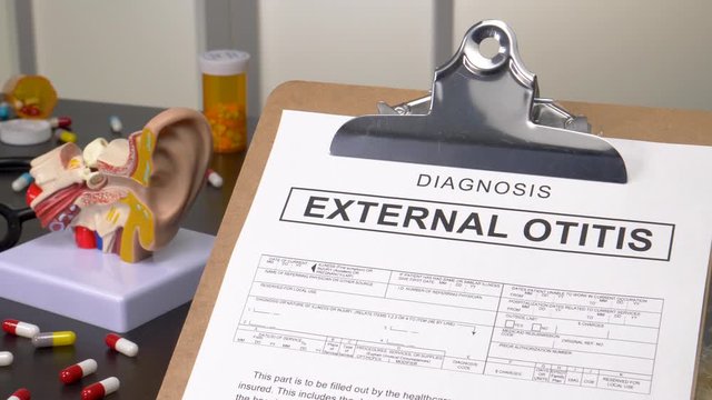 External Otitis patient diagnosis on a medic office with pills, stethoscope and anatomy models. Camera panning reveling the notebook with the medical record copy.