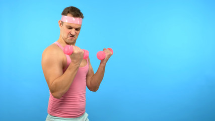 Playful handsome man in a pink shirt is engaged in fitness with pink dumbbells. Bright Fitness. Sports Fashion Accessories