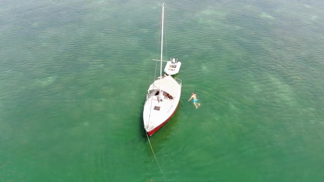 Zwei junge M&auml;nner schwimmen um ein Boot mit Beiboot herum 