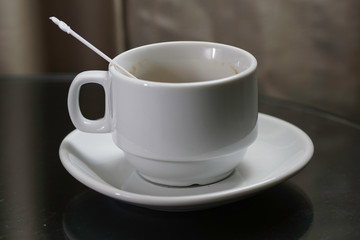 A white coffee cup with  plastic spoon  over black background.