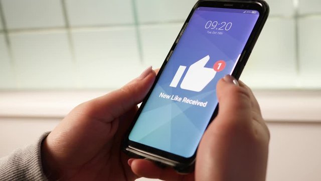 Woman holding her mobile phone and receiving a social media thumbs up like.