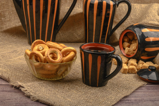Small bagels, brown sugar, a mug of tea and ceramic dishes on a background of rough homespun fabric close-up.