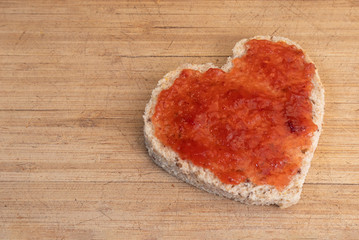Slice of bread in heart shape. Healthy whole wheat bread with strawberry jam on wood cutting board. Concept about love. Copy space.