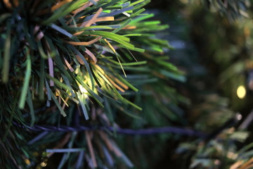 Green leaves are on branch of artificial pine tree, light is on branch.