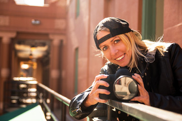 A young blonde girl smiles and holds a DSLR camera with a wide angle lens