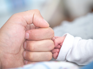 A father and newborn son touch knuckles as the baby's tiny fingers juxtapose against his dad's large clenched fist.