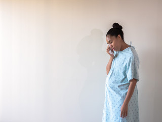 A young postpartum mixed race African American woman wearing a hospital gown or robe hunches over and looks down as she dries her eyes from tears of sadness or depression from a loss. - Powered by Adobe