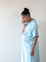 A young postpartum mixed race African American woman wearing a hospital gown or robe hunches over...