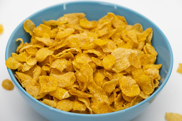 Golden cornflakes in the blue bowl isolated on white background