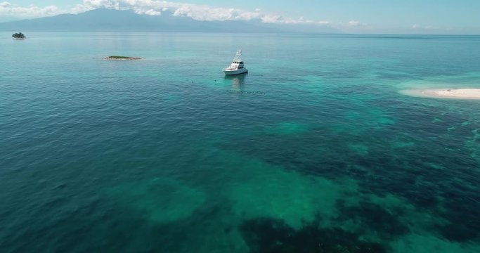 Aerial forward, over snorklers in tropical reef water, next to luxury yacht, Roatan