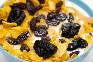 Cornflakes resin and dry prunes with fresh milk in the blue bowl on white background