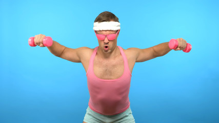 Playful handsome man in a pink shirt is engaged in fitness with pink dumbbells. Bright Fitness. Sports Fashion Accessories