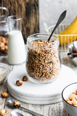 Chocolate banana granola with nuts in a glass jar on a light background