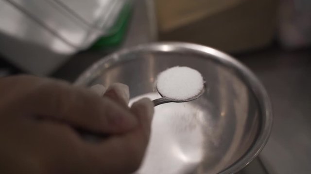 Adding about a tablespoon of salt into a metal bowl full of other spices. Taken at a higher frame rate and has been converted to a slow motion video clip.