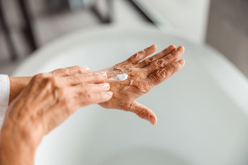 Elderly lady applying moisturizing cream on hand